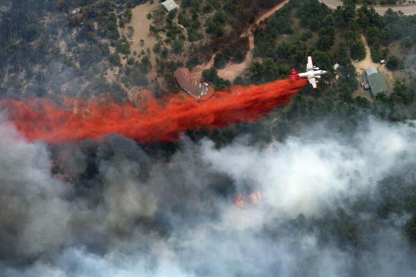 FILE - An aircraft lays down a line of fire retardant between a wildfire and homes in the dry, densely wooded Black Forest area northeast of Colorado Springs, Colo., on June 13, 2013. A federal judge said Friday, May 26, 2023, that chemical retardant dropped on wildfires by the U.S. Forest Service is polluting streams in western states in violation of federal law, but said it can keep being use to fight fires. (AP Photo/John Wark, File)