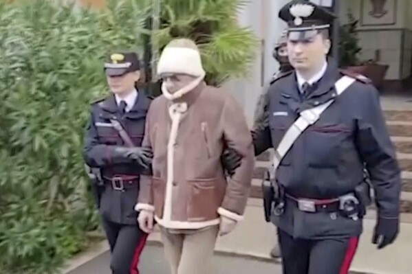This image taken from an Italian Carabinieri handout video dating Jan. 16, 2023 shows Matteo Messina Denaro, center, a top Mafia boss, being escorted from a Carabinieri police station shortly after his arrest, in Palermo, southern Italy. Messina Denaro, a convicted mastermind of some of the Sicilian Mafia’s most heinous slayings, died on Monday, Sept. 25, 2023, in a hospital prison ward, several months after being captured as Italy’s No. 1 fugitive and following decades on the run, Italian prosecutors said. (Carabinieri via AP)