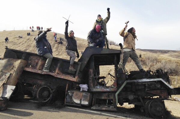 FILE - Protesters against the Dakota Access oil pipeline stand on a burned-out truck, Nov. 21, 2016, near Cannon Ball, N.D. North Dakota is set to take the federal government to trial on Thursday, Feb. 15, 2024, for the costs of responding to the Dakota Access Pipeline protests, the culmination of an unusual and drawn-out court fight. (AP Photo/James MacPherson, File)
