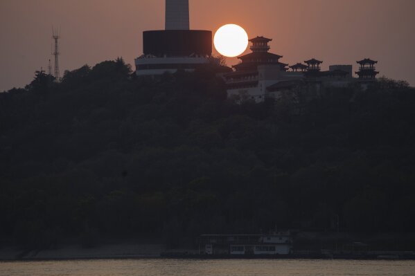 The sun sets over the television tower along the Yangtze River in Wuhan in central China's Hubei province on Wednesday, April 8, 2020. Streets in the city of 11 million people were clogged with traffic and long lines formed at the airport, train and bus stations as thousands streamed out of the city to return to homes and jobs elsewhere. Yellow barriers that had blocked off some streets were gone, although the gates to residential compounds remained guarded. (AP Photo/Ng Han Guan)