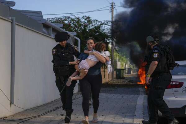FILE - Israeli police officers evacuate a woman and a child from a site hit by a rocket fired from the Gaza Strip, in Ashkelon, southern Israel, Saturday, Oct. 7, 2023. (AP Photo/Tsafrir Abayov, File)