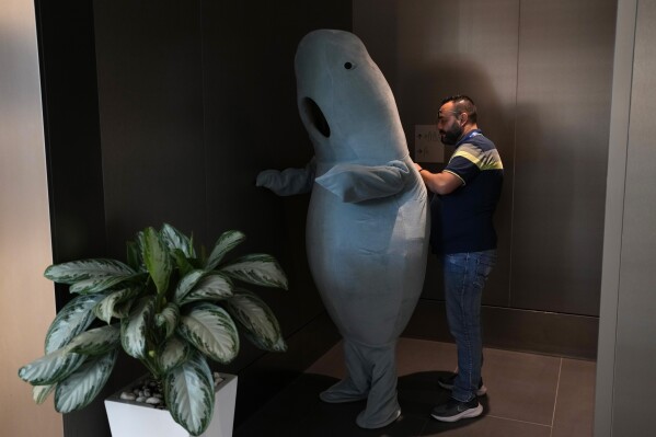 A person is helped in a dugong costume at the COP28 U.N. Climate Summit, Dec. 5, 2023, in Dubai, United Arab Emirates. (AP Photo/Rafiq Maqbool)