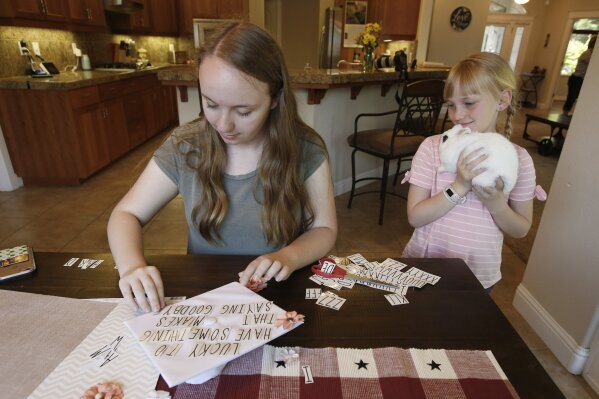 Emilee Taylor a senior at Paradise High School, decorates her graduation cap as her younger sister Baylee, 10, with her pet rabbit, Sebby, watches, at their home in Chico, Calif., Wednesday, June 5, 2019. After the Camp Fire destroyed their home in Paradise, they lived with Emilee's grand parents until they found their own home in Chico. Taylor and the rest of the Paradise High School Class of 2019 are graduating Thursday. (AP Photo/Rich Pedroncelli)