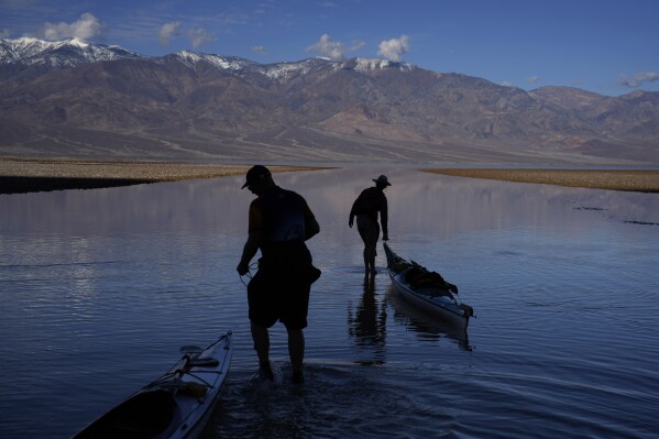 Brian Nelson, left, and Kathleen Nelson, right, both of Bishop, Calif., pull kayaks into water at Badwater Basin, Thursday, Feb. 22, 2024, in Death Valley National Park, Calif. The basin, normally a salt flat, has filled from rain over the past few months. (AP Photo/John Locher)