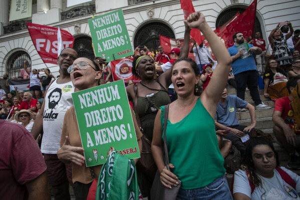 Women shout slogans while holding signs with a message in Portuguese that says: 