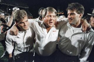 FILE - Miami coach Jimmy Johnson, center, is hugged by his sons, Chad, left, and Brent, rightk, while walking off the field following the team's win over Nebraska in the Orange Bowl college football game in Miami, Jan. 2, 1989. Johnson won two Super Bowls as coach of the Dallas Cowboys and a national championship at Miami. In his view, Johnson’s biggest success has nothing to do with football. The 79-year-old Johnson describes in “Swagger,” his memoir that released on Tuesday, how his addiction to football and winning caused him to never have a family dinner. His two sons played football but Dad never saw them play a full game.  (AP Photo/Chris O'Meara, File)
