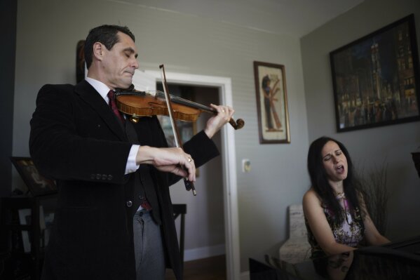Musicians David Shenton and Erin Shields perform inside their home in the Queens borough of New York on March 30, 2021. The married couple have led virtual concerts from their living room to raise thousands of dollars for the Mosaic West Queens Church food pantry, where they volunteer every weekend. (AP Photo/Emily Leshner)