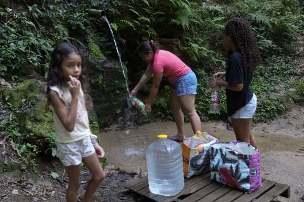 Residents collect drinking water that falls naturally down a mountain in the Rocinha favela of Rio de Janeiro, Brazil, Monday, March 18, 2024. (AP Photo/Silvia Izquierdo)