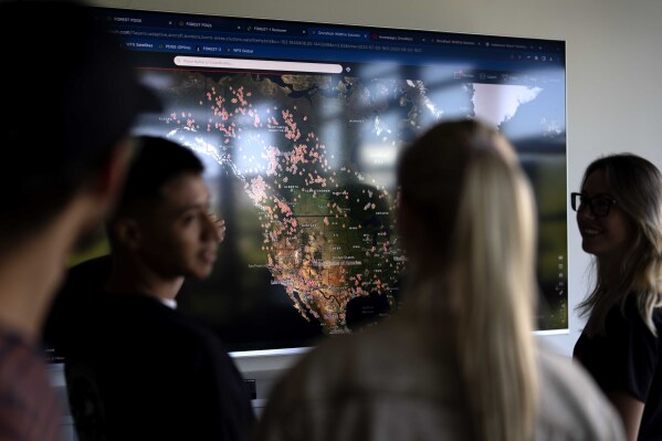 Employees of German startup OroraTech stand in front of a screen showing wildfires in Canada and the United States via satellites in Munich, Germany, Thursday, Sept. 13, 2023. The Munich-based company analyzes satellite images with artificial intelligence. The AI also takes into account factors like the type and condition of vegetation in the area and humidity levels, to detect and identify those flareups that have the potential to spawn devastating megafires. (AP Photo/Matthias Schrader)