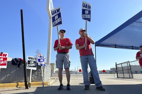 Striking United Auto Workers member Chris Jedrzejek, right, and his father picket outside Ford Motor Co.'s Michigan Assembly Plant Monday, Oct. 2, 2023, in Wayne, Mich. Electric vehicles and their potential impact on job security have become central to negotiations in the U.S. autoworkers strike. (AP Photo/Mike Householder)