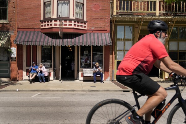 People enjoy ice cream outside a downtown business as a cyclist rides past Wednesday, May 22, 2024, in Hannibal, Mo. Devastating flooding, driven in part by climate change, is taking an especially damaging toll on communities that once thrived along the banks of the Mississippi River. (AP Photo/Jeff Roberson)