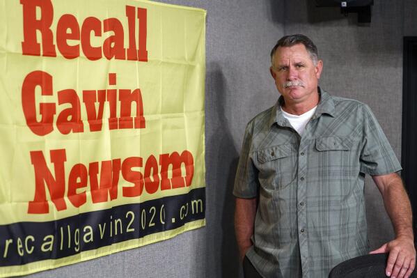 FILE — In this March 27, 2021, file photo Orrin Heatlie, the main organizer for the Recall of California Gov. Newsom campaign, poses with a banner before recording a radio program at KABC radio station studio in Culver City, Calif. Heatlie, the Republican activist who launched the recall efforts, has filed a lawsuit Friday, July 30, 2021, to prohibit Newsom from calling the effort a "Republicans recall" in the state's official voter guide. (AP Photo/Damian Dovarganes, File)
