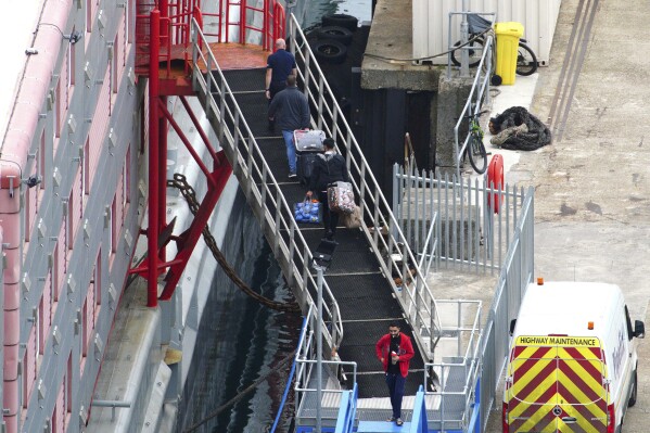 People board the Bibby Stockholm accommodation barge at Portland Port in Dorset, England, Tuesday Aug. 8, 2023. Britain’s government on Monday, Aug. 14, 2023, rejected claims that it had been slow to evacuate asylum seekers from a barge moored off the south coast of England once traces of the bacteria that causes Legionnaire’s disease were found in the ship’s water system. (Ben Birchall/PA via AP)