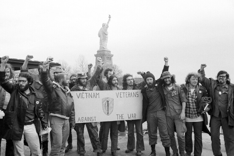 FILE - Members of the Vietnam Veterans Against the War raise clenched fists after ending their 40-hour occupation of State of Liberty, which can be seen behind them, Dec. 28, 1971. They’re hallmarks of American history: protests, rallies, sit-ins, marches, disruptions. They date from the early days of what would become the United States to the sights and sounds currently echoing across the landscapes of the nation’s colleges and universities. (AP Photo/Anthony Camerano, File)