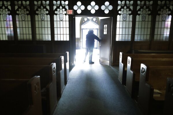 In this Saturday, Nov. 9, 2019 photo, Rev. Mark Stelzer, administrator of St. Jerome's Parish, in Holyoke, Mass., opens doors to the Catholic church before offering Mass. Stelzer, also a professor and chaplain at College of Our Lady of the Elms, in Chicopee, Mass., lives alone in the rectory at St. Jerome's while serving as spiritual leader to the 500 families in the Catholic parish. (AP Photo/Steven Senne)