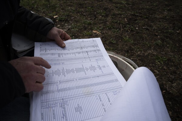 Eric Cordingley looks at his records while searching for the graves of those who died at Morningside Hospital at Multnomah Park Cemetery on Wednesday, March 13, 2024, in Portland, Ore. (AP Photo/Jenny Kane)