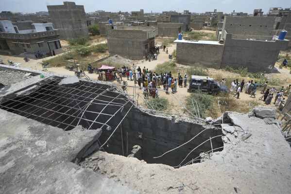 A big hole is seen on a rooftop of a house suspected to have been damaged in Indian drone attack as residents, behind, gather near a cordoned off site, where Pakistan's air defense system shot down a suspected Indian drone in Karachi, Pakistan, Thursday, May 8, 2025. (AP Photo/Fareed Khan)