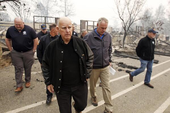 FILE - Former California Gov. Jerry Brown, center, and former Interior Secretary Ryan Zinke, second from right, tour the Camp-fire ravaged Paradise Elementary School in Paradise, Calif., on Nov. 14, 2018. Brown has called California's mega fires "the new abnormal" as climate change turns the state warmer and drier. With the help of Ken Pimlott, the former chief of the California Department of Forestry and Fire Protection, Brown convened a group at his rural Colusa County ranch in September 2021, to discuss what could be done to save California's forests. (AP Photo/Rich Pedroncelli, File)