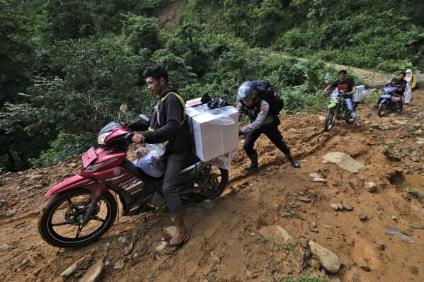 A police officer assists an electoral worker to drive his motorbike up a hill as they distribute ballot boxes and other election paraphernalia to polling stations in remote villages ahead of the Feb. 14 election in Maros, Indonesia, Tuesday, Feb. 13, 2024. Indonesia, the world's third-largest democracy, will open its polls on Wednesday to nearly 205 million eligible voters in presidential and legislative elections, the fifth since Southeast Asia's largest economy began democratic reforms in 1998. (AP Photo/Masyudi S. Firmansyah)