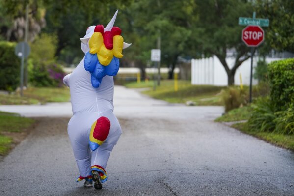 Corey Jurgensen has been wearing an inflatable unicorn costume during runs several times a week to cheer up others during this time of isolation but finds it therapeutic for herself as well to run through her Seminole Heights neighborhood wearing a costume, Thursday, April 16, 2020 in Tampa, Fla. (Martha Asencio Rhine/Tampa Bay Times via AP)