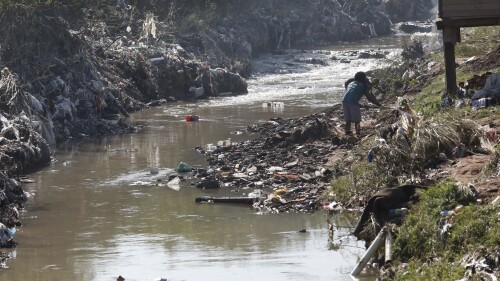 A woman on the banks of a strong-flowing stream near Durban, South Africa, Wednesday, June 28, 2023. Authorities say seven people have died and another seven are missing after floods in and surrounding area. (AP Photo)