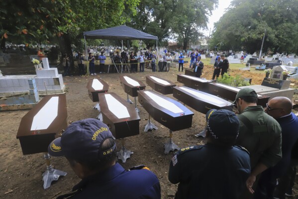 Authorities stand next to the nine coffins that contain the remains of unidentified migrants, at the Sao Jorge cemetery, in Belem, Para state, Brazil, Thursday, April 25, 2024. The bodies of nine migrants found on an African boat off the northern coast of Brazil's Amazon region were buried Thursday with a solemn ceremony. (AP Photo/Paulo Santos)