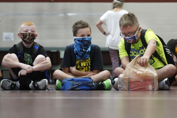 FILE - In this Aug. 5, 2020, file photo, wearing masks to prevent the spread of COVID19, elementary school students wait for classes to begin in Godley, Texas. As schools reopen around the country, their ability to quickly identify and contain coronavirus outbreaks before they get out of hand is about to be put to the test. (AP Photo/LM Otero, File)