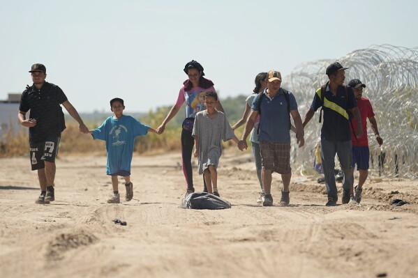 Migrantes que cruzaron a Estados Unidos desde México pasan junto a alambres con concertinas, o cuchillas, a orillas del Río Bravo, mientras caminan hacia un centro de procesamiento, el 21 de septiembre de 2023, en Eagle Pass, Texas. (AP Foto/Eric Gay)