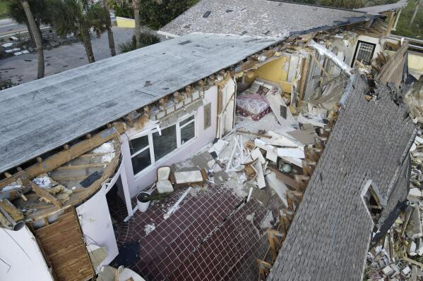 A bed and chairs are seen inside a home that half collapsed after the sand supporting it was swept away, following the passage of Hurricane Nicole, Saturday, Nov. 12, 2022, in Wilbur-By-The-Sea, Fla. (AP Photo/Rebecca Blackwell)