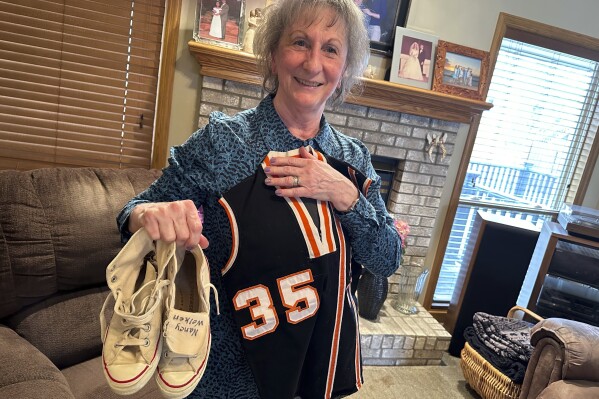 Nancy Schmitz poses with the jersey and sneakers she wore when she played six-on-six basketball at Elk Horn-Kimballton High School in the 1960s at her home in La Vista, Neb., Monday, March 4, 2024. Schmitz, then Nancy Wolken, was a third-team all-state pick in 1968. (AP Photo/Eric Olson)