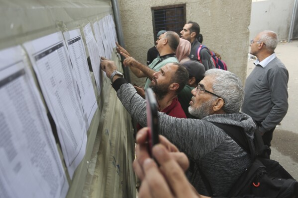 Palestinians check lists with the names of people allowed to cross to Egypt from the Gaza Strip in Rafah, Monday, Nov. 13, 2023. (AP Photo/Hatem Ali)