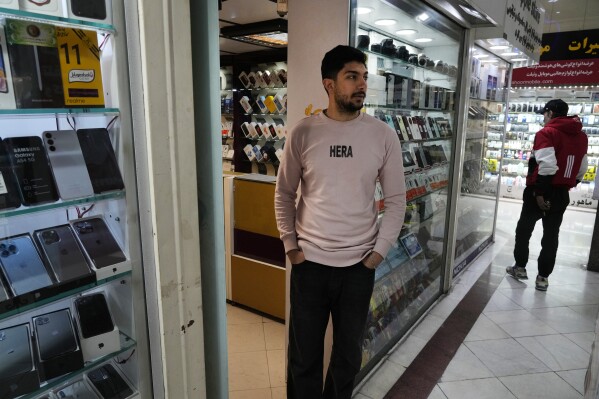 A cellphone vendor waits for customer as he stands outside his shop in downtown Tehran, Iran, Wednesday, Feb. 21, 2024. Even though Supreme Leader Ayatollah Ali Khamenei has denounced American luxury goods amid years of tensions with the West, consumers still want the phones and the prestige associated with them. (AP Photo/Vahid Salemi)