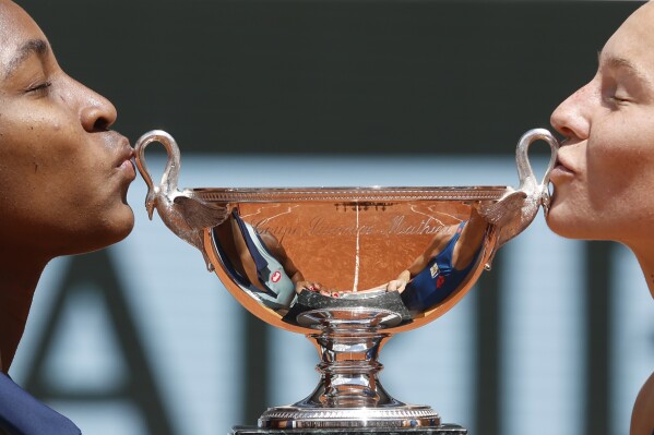 Coco Gauff of the U.S., left, and Katerina Siniakova of the Czech Republic kiss the trophy as they won the women's doubles final match of the French Open tennis tournament against Italy's Sara Errani and Jasmine Paolini at the Roland Garros stadium in Paris, Sunday, June 9, 2024. (AP Photo/Jean-Francois Badias)