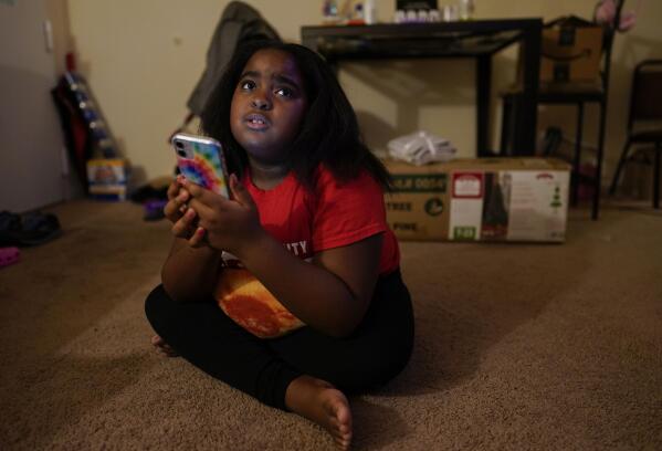 Brooklynn Chiles, 8, glances up from her smart phone at home where she lives with her mother, Danielle Mitchell in Washington, Sunday, Jan. 9, 2022. Brooklynn lost her father to COVID-19 last year and has tested positive three times herself. She is part of a NIH-funded multi-year study at Children's National Hospital to look at impacts of COVID-19 on children's physical health and quality of life. (AP Photo/Carolyn Kaster)