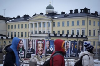 People walk by election posters with the Presidential Palace in the background, in Helsinki, Finland, Saturday, Jan. 27, 2024, ahead of the Finnish presidential election on Sunday. (AP Photo/Sergei Grits)