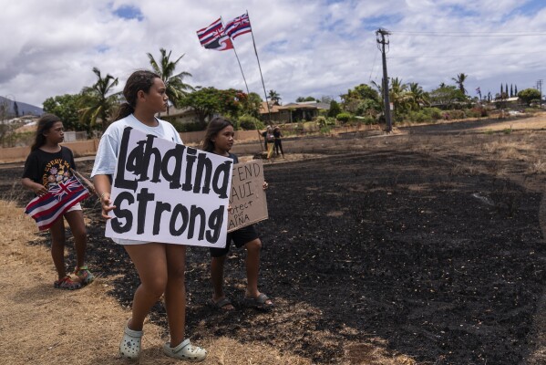 Children hold signs and a Hawaiian flag while waiting for the arrival of President Joe Biden outside the Lahaina Civic Center in Lahaina, Hawaii, Monday, Aug. 21, 2023. (AP Photo/Jae C. Hong)