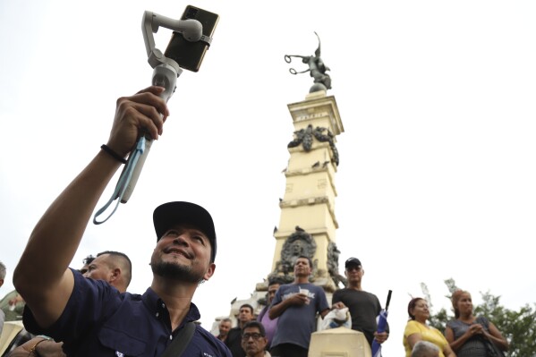 Douglas Guzman takes video with his smartphone at Liberty Plaza in San Salvador, El Salvador, Saturday, June 24, 2023. Guzmán is part of a network of social media personalities acting as a megaphone for, and cashing in on, El Salvador President Nayib Bukele's message. (AP Photo/Salvador Melendez)