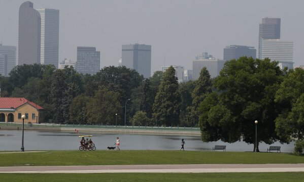 
              A smoky haze obstructs the view of the skyscrapers and Rocky Mountains that usually can be seen as a backdrop to the city as bicyclists and runners pass the lake in City Park, Monday, Aug. 20, 2018, in Denver. Smoke from the countless wildfires burning in western Canada as well as the American West has forced the issuance of air quality alerts across the region. (AP Photo/David Zalubowski)
            