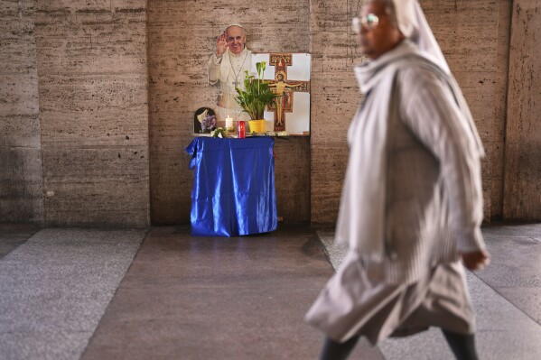 A cardboard cutout of the late Pope Francis is placed next to candles and flowers outside St. Peter's Square at the Vatican, Tuesday, April 22, 2025. (AP Photo/Francisco Seco)