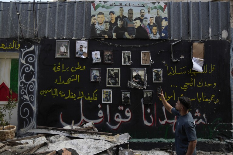 A man takes a picture of a wall displaying photos of Palestinians, who died during previous clashes, following an Israeli military operation in the West Bank refugee camp of Al-Faraa, Thursday, Aug. 29, 2024. (AP Photo/Nasser Nasser)