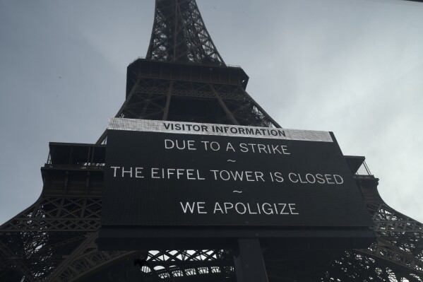 A board warns about a strike at the Eiffel Tower, Wednesday, Dec. 27, 2023 in Paris. The Eiffel Tower was shut down to visitors Wednesday because of a strike over contract negotiations, the day the Paris monument marks 100 years since the death of its creator, Gustave Eiffel. Tourists can still access the glass-enclosed esplanade beneath the tower, but access to the 300-meter (984-foot) landmark itself is closed until further notice, (AP Photo/Lewis Joly)