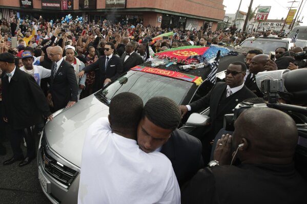 FILE - In this April 11, 2019 file photo, two men embrace as a hearse carrying the casket of slain rapper Nipsey Hussle passes through a dense crowd in Los Angeles. The 25-mile procession traveled through the streets of South Los Angeles after his memorial service, including a trip past Hussle's clothing store, The Marathon, where he was gunned down March 31. A year after Hussle's death, his popularity and influence are as strong as ever. He won two posthumous Grammys in January, he remains a favorite of his hip-hop peers and his death has reshaped his hometown of Los Angeles in some unexpected ways.(AP Photo/Jae C. Hong, File)