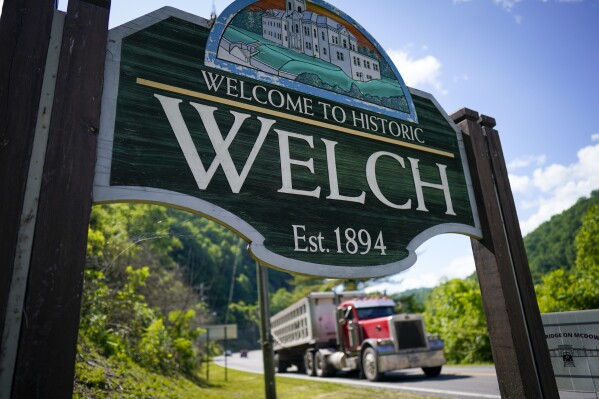FILE- A coal truck drives past the welcome sign on Thursday, June 1, 2023, in Welch, W.Va. Authorities say 11 suspects have been arrested in an investigation into illegal drugs allegedly being delivered by drones into a federal prison in southern West Virginia. Another man who fled officers was later found dead. (AP Photo/Chris Carlson, File)