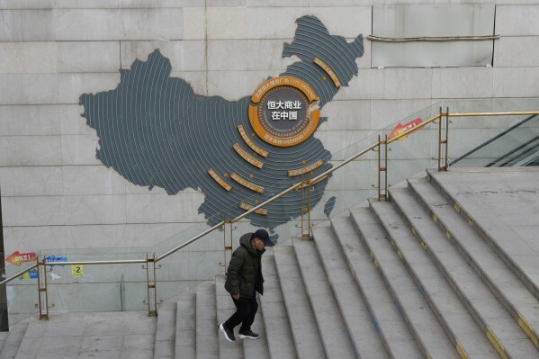 FILE - A man walks past a depiction of Evergrande properties across a China map at a partially shuttered Evergrande commercial complex in Beijing, on Jan. 29, 2024. Troubled property developer China Evergrande Holding says Beijing’s stock watchdog has fined it 4.2 billion yuan ($333.4 million) for allegedly falsifying its revenue, among other allegations. (AP Photo/Ng Han Guan, File)