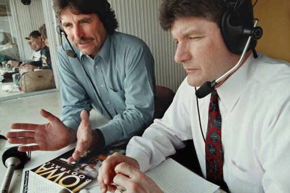 FILE - University of Iowa football radio color commentator Ed Podolak, left, works with play-by-play announcer Gary Dolphin before the Iowa spring football game, April 19, 1997, in Iowa City, Iowa. Longtime Iowa football broadcaster Ed Podolak has announced he will move out of the radio booth this season and limit his appearances to pregame shows and podcasts. Podolak played quarterback and running back for the Hawkeyes before he became a fixture at running back for the Kansas City Chiefs from 1969-77. Podolak was a color commentator for NBC and ESPN before he joined the Iowa radio broadcast crew in 1982. (Harry Baumert/The Des Moines Register via AP, File)