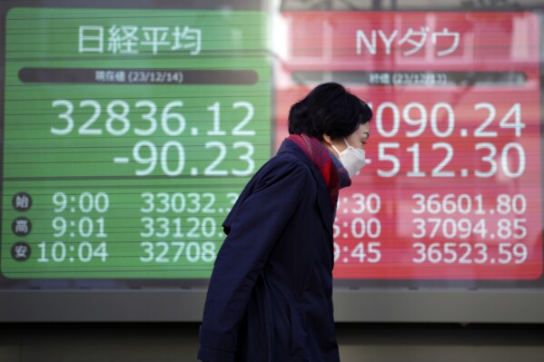 A person walks near an electronic stock board showing Japan's Nikkei 225, left, and New York Dow indexes at a securities firm Thursday, Dec. 14, 2023, in Tokyo. Shares are mostly higher in Asia after a powerful rally across Wall Street sent the Dow Jones Industrial Average to a record high as the Federal Reserve indicated that interest rate cuts are likely next year.(AP Photo/Eugene Hoshiko)