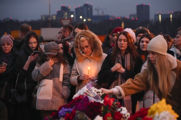 People lay flowers and light candles standing next to the Crocus City Hall, on the western edge of Moscow, Russia, Saturday, March 23, 2024. (AP Photo/Alexander Zemlianichenko)