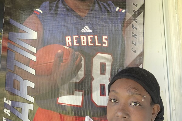 FILE - Ericka Lotts stands next to a poster of her son, Derontae Martin, from his high school football playing days, Sept. 17, 2021, at her home in Ferguson, Mo. Martin died of a self-inflicted gunshot wound inside a rural Missouri home, not at the hands of the white homeowner who had a history of racist social media postings, an FBI official told The Associated Press on Wednesday, April 24, 2024. (AP Photo/Jim Salter, File)