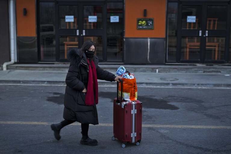 A woman with her luggage walks by a restaurant closed for the upcoming Lunar New Year as she leaves a village to catch her transport on the outskirt of Beijing, Tuesday, Feb. 6, 2024. Widespread snowfall and freezing weather continued in central and eastern China disrupting transport and stranding travelers amid the annual Lunar New Year travel rush. (AP Photo/Andy Wong)