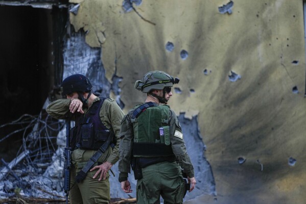 FILE - Israeli soldiers walk past houses destroyed by Hamas militants in Kibbutz Be'eri, Israel, Saturday, Oct. 14, 2023. Now 100 days old, the latest Israel-Hamas war is by far the longest, bloodiest, and most destructive conflict between the bitter enemies. The fighting erupted on Oct. 7, 2023 when Hamas carried out a deadly attack in southern Israel. Since then, Israel has relentlessly pounded the Gaza Strip with airstrikes and a ground offensive that have wrought unprecedented destruction, flattening entire neighborhoods. . (AP Photo/Ariel Schalit, File)